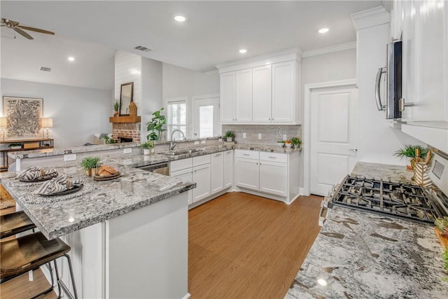 9868 Albert Dr, Iola, TX 77861 - kitchen with a peninsula, a ceiling fan, a brick fireplace, backsplash, and white cabinets