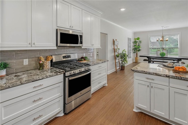9868 Albert Dr, Iola, TX 77861 - kitchen with appliances with stainless steel finishes, backsplash, light wood-style flooring, white cabinetry, and ornamental molding