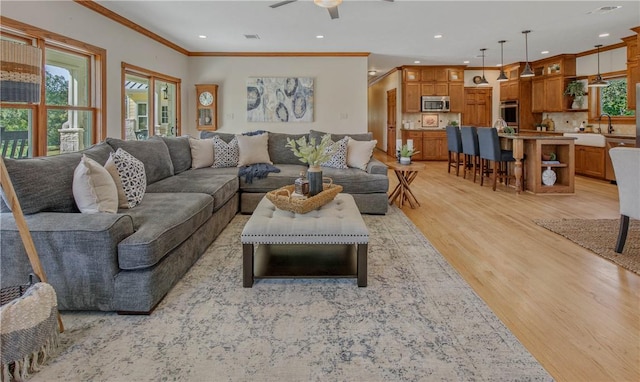 living room featuring light hardwood / wood-style flooring, ceiling fan, crown molding, and sink