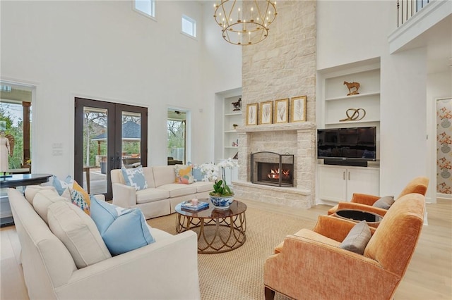 living area with light wood finished floors, baseboards, french doors, a stone fireplace, and built in shelves