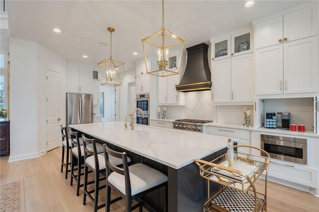 kitchen with stainless steel appliances, premium range hood, a center island with sink, and white cabinetry