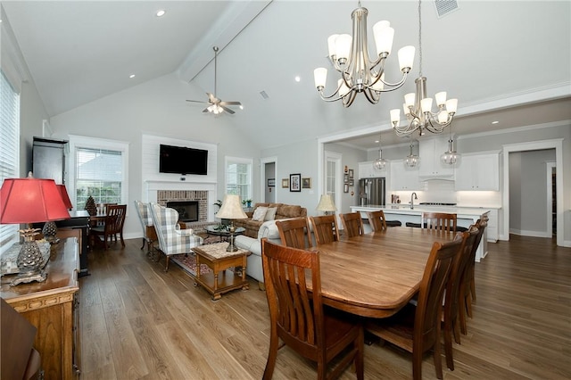 dining area featuring high vaulted ceiling, ceiling fan with notable chandelier, wood finished floors, beamed ceiling, and visible vents