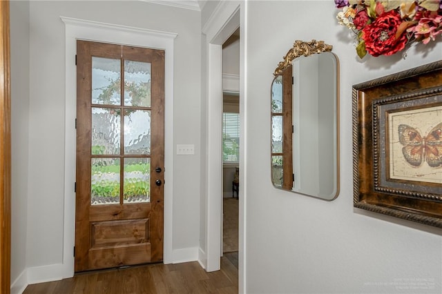 doorway to outside featuring baseboards, crown molding, and wood finished floors