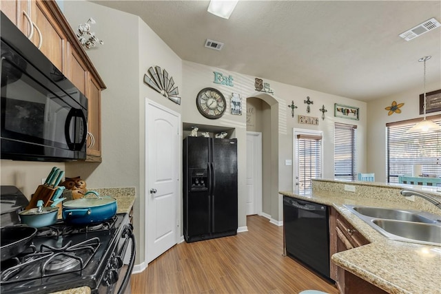 kitchen featuring light stone countertops, sink, light hardwood / wood-style floors, decorative light fixtures, and black appliances