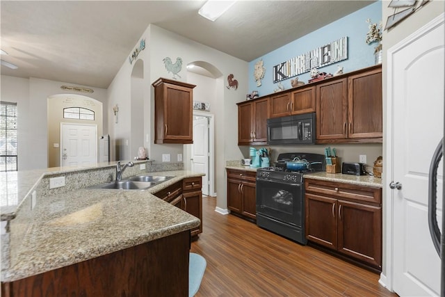 kitchen featuring dark wood-type flooring, light stone counters, sink, and black appliances