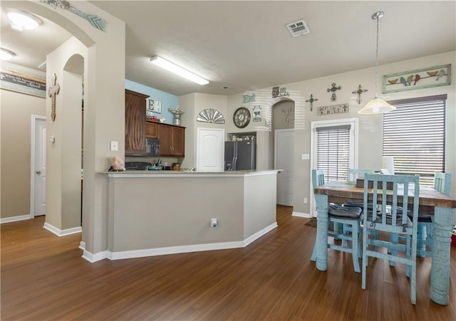 kitchen featuring kitchen peninsula, pendant lighting, black appliances, and dark hardwood / wood-style floors