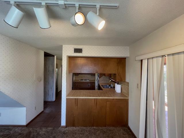 kitchen with visible vents, wallpapered walls, a sink, a textured ceiling, and brown cabinets