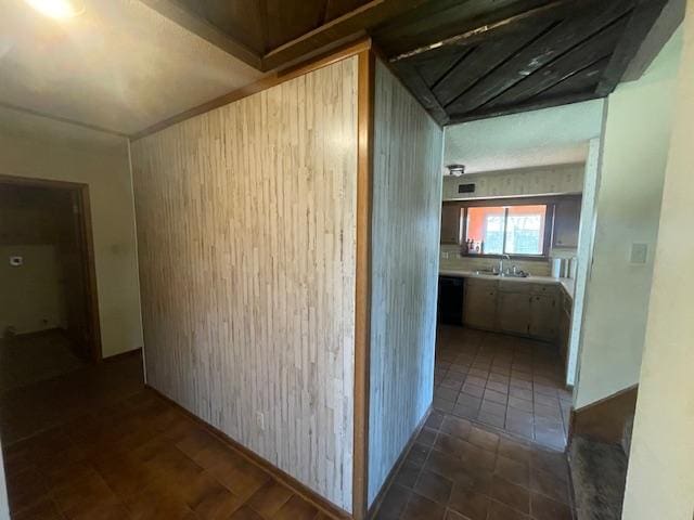 corridor with wood walls, dark tile patterned flooring, and a sink