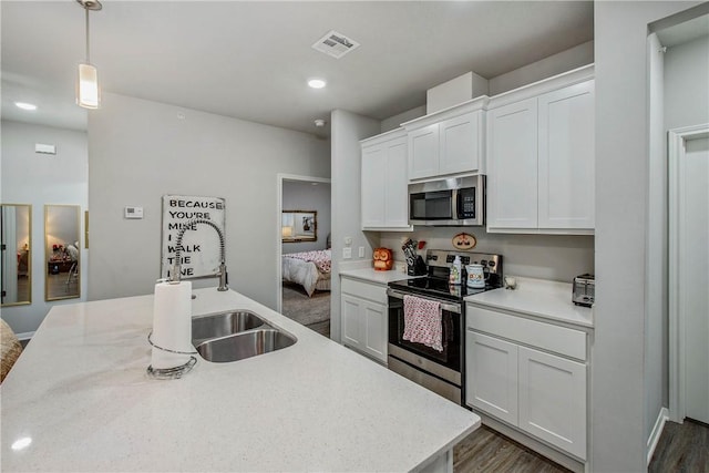 kitchen with stainless steel appliances, light countertops, white cabinets, a sink, and an island with sink