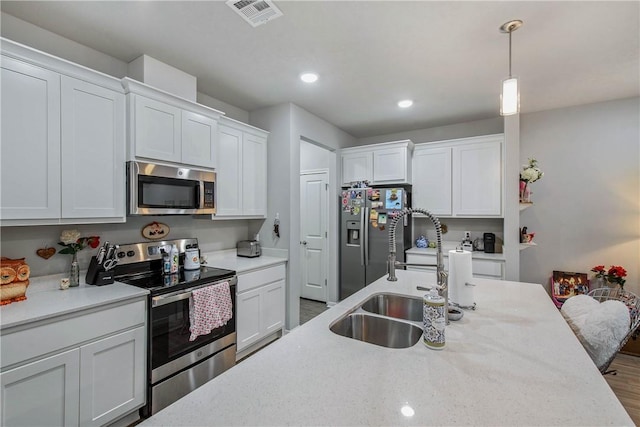 kitchen with stainless steel appliances, a sink, visible vents, white cabinets, and decorative light fixtures