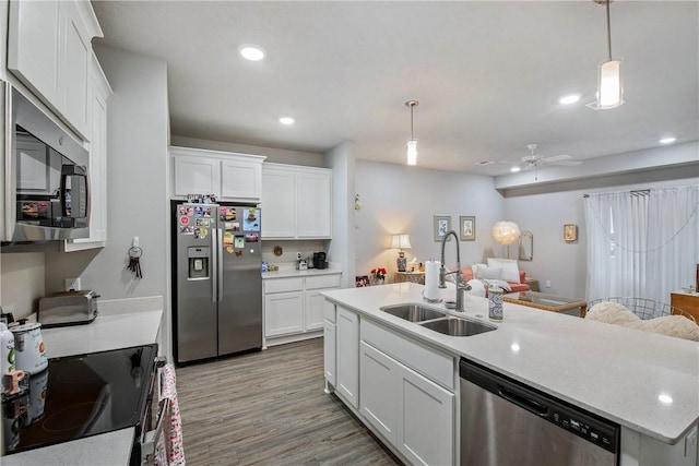 kitchen with wood finished floors, a sink, white cabinets, open floor plan, and appliances with stainless steel finishes