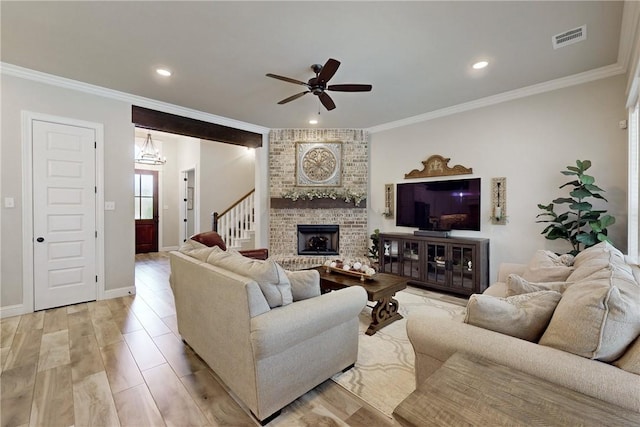 living room with ceiling fan with notable chandelier, a brick fireplace, crown molding, and light hardwood / wood-style flooring