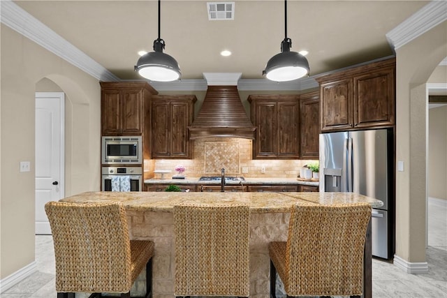 5104 Stonewater Loop, College Station, TX 77845 - kitchen featuring appliances with stainless steel finishes, custom range hood, arched walkways, a kitchen island with sink, and crown molding