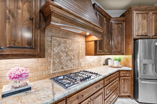 5104 Stonewater Loop, College Station, TX 77845 - kitchen with appliances with stainless steel finishes, tasteful backsplash, light stone counters, premium range hood, and ornamental molding