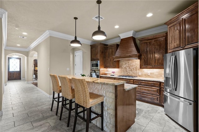 5104 Stonewater Loop, College Station, TX 77845 - kitchen with stainless steel appliances, arched walkways, custom range hood, a center island with sink, and tasteful backsplash