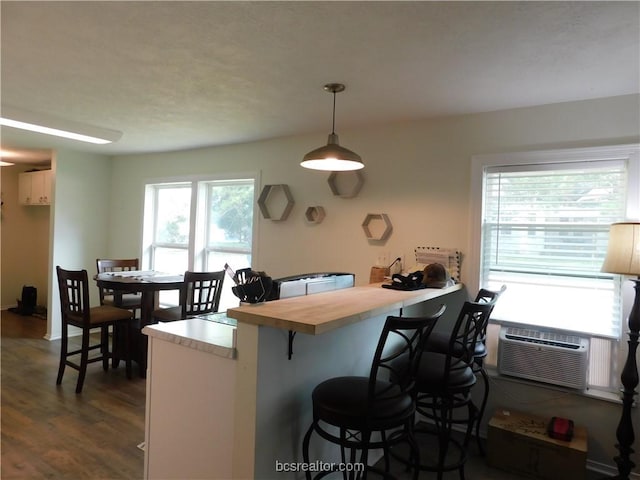1117 Sycamore St, Navasota, TX 77868 - kitchen featuring dark wood-type flooring, an AC wall unit, decorative light fixtures, a breakfast bar, and wood counters
