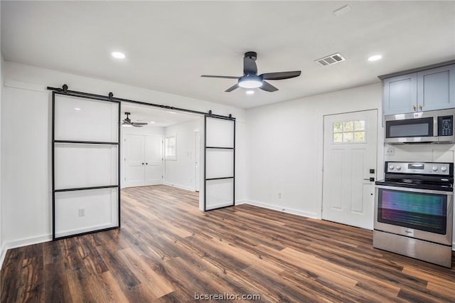 kitchen featuring appliances with stainless steel finishes, gray cabinetry, ceiling fan, dark wood-type flooring, and a barn door