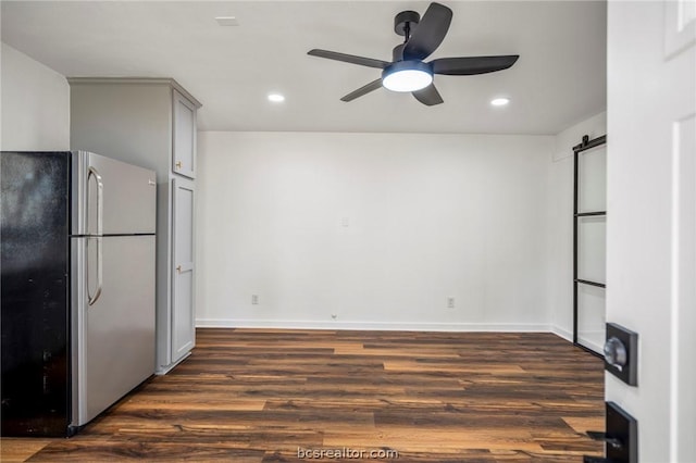 kitchen with ceiling fan, gray cabinets, a barn door, dark hardwood / wood-style flooring, and stainless steel refrigerator