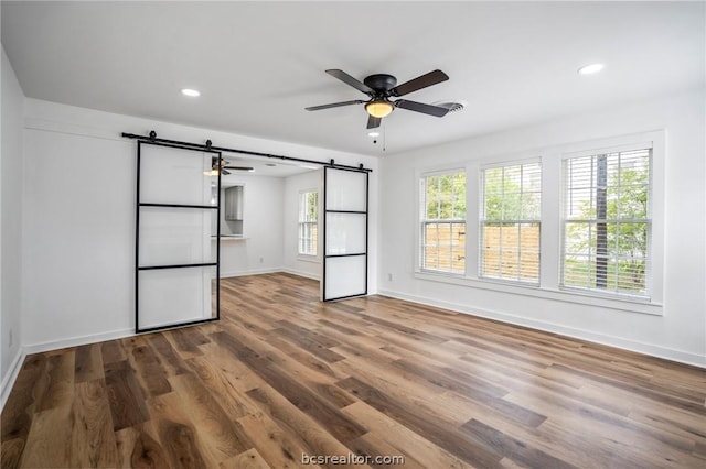 unfurnished bedroom with hardwood / wood-style floors, ceiling fan, and a barn door