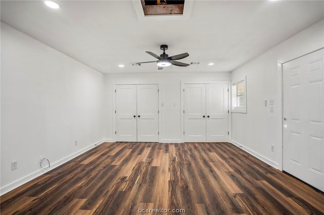 unfurnished bedroom featuring ceiling fan, dark wood-type flooring, and two closets