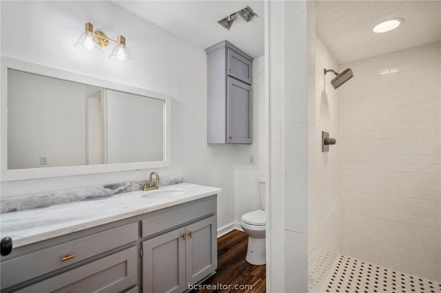 bathroom featuring tiled shower, toilet, vanity, and hardwood / wood-style flooring