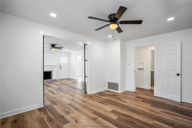 empty room with ceiling fan, hardwood / wood-style floors, and a brick fireplace