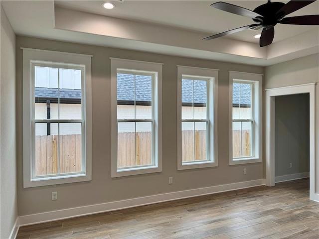 unfurnished room featuring a tray ceiling, light hardwood / wood-style floors, and ceiling fan