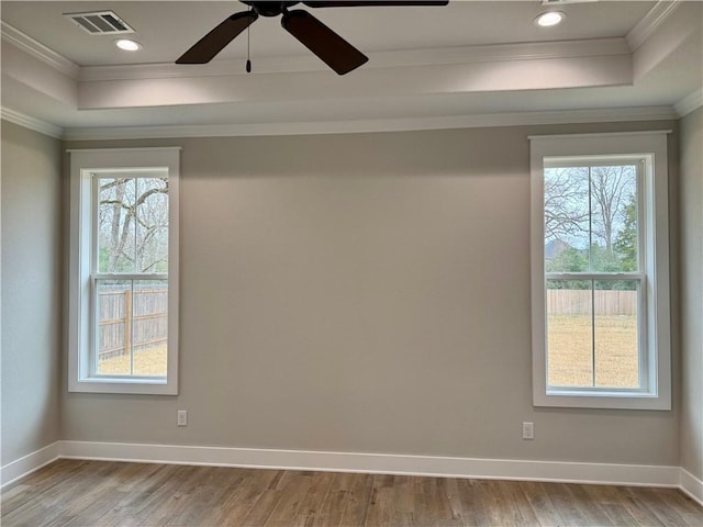 empty room featuring a raised ceiling, ornamental molding, and light wood-type flooring