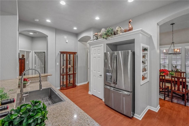 kitchen with stainless steel refrigerator with ice dispenser, sink, light stone counters, a chandelier, and pendant lighting