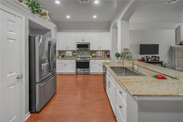 kitchen featuring appliances with stainless steel finishes, tasteful backsplash, white cabinetry, sink, and light stone countertops