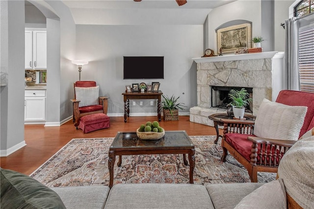 living room featuring ceiling fan, lofted ceiling, a fireplace, and light wood-type flooring