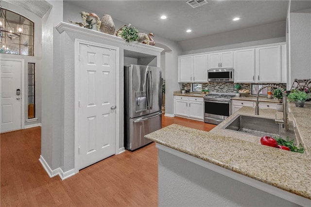 kitchen featuring white cabinetry, sink, backsplash, stainless steel appliances, and light stone countertops