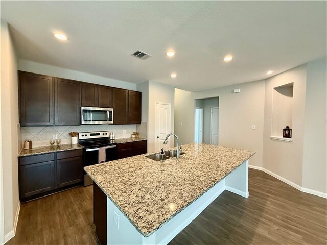 4704 Los Pines Way, Bryan, TX 77807 - kitchen with stainless steel appliances, a sink, dark wood-style flooring, baseboards, and an island with sink