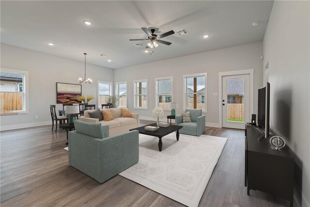 living room with a wealth of natural light, ceiling fan with notable chandelier, and dark hardwood / wood-style floors