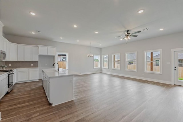 kitchen with decorative backsplash, appliances with stainless steel finishes, hardwood / wood-style flooring, decorative light fixtures, and an island with sink