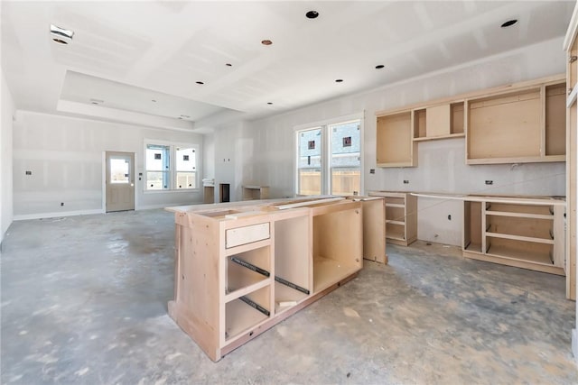 kitchen with a center island, a tray ceiling, light brown cabinetry, and concrete floors