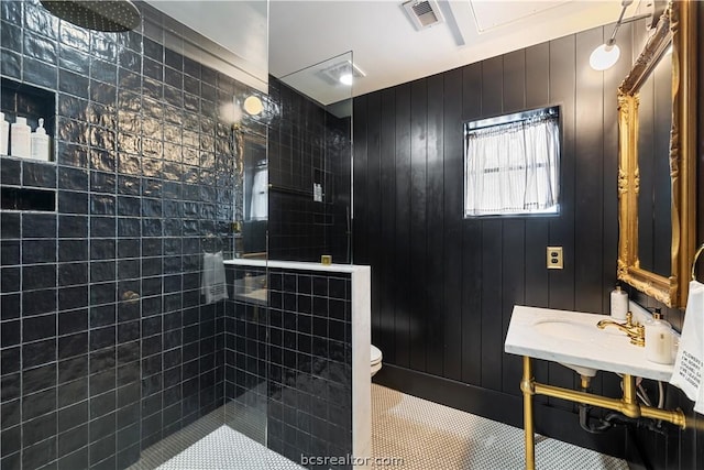 bathroom featuring a tile shower, wood walls, tile patterned flooring, and toilet