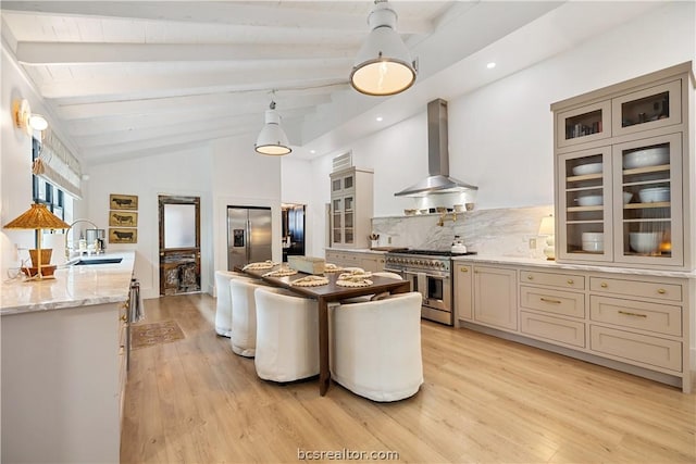 kitchen featuring sink, wall chimney exhaust hood, stainless steel appliances, vaulted ceiling with beams, and light stone counters