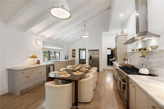 kitchen featuring appliances with stainless steel finishes, light wood-type flooring, light stone counters, wall chimney range hood, and lofted ceiling with beams