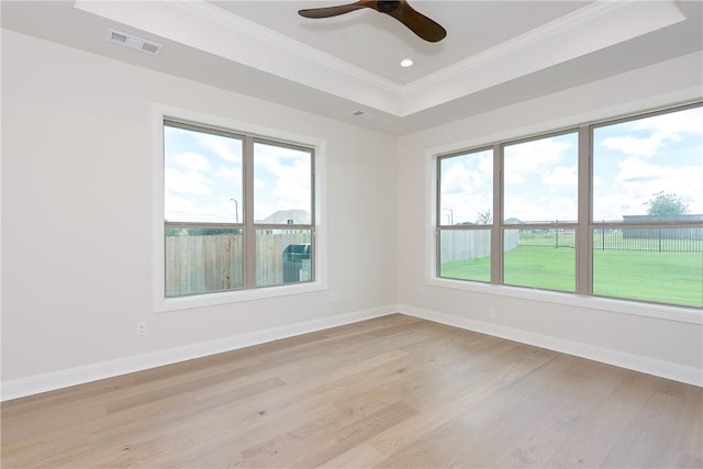 empty room featuring light wood-type flooring, a tray ceiling, ceiling fan, and ornamental molding