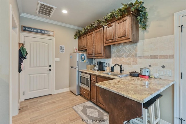 kitchen featuring crown molding, sink, light hardwood / wood-style flooring, light stone counters, and stainless steel appliances