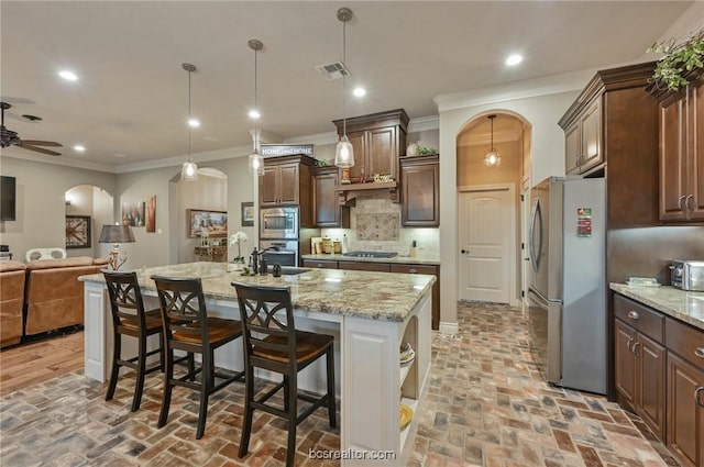 kitchen with decorative backsplash, appliances with stainless steel finishes, a center island with sink, decorative light fixtures, and a breakfast bar area