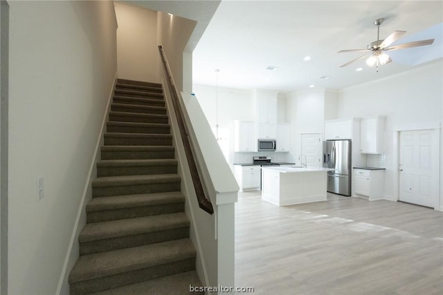 stairway featuring ceiling fan, hardwood / wood-style floors, ornamental molding, and sink