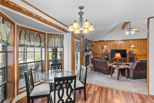 dining area with lofted ceiling with beams, a large fireplace, wood finished floors, and ceiling fan with notable chandelier