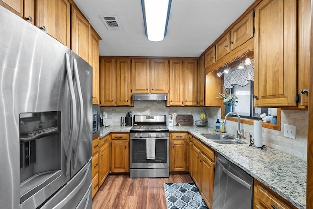 kitchen featuring under cabinet range hood, a sink, visible vents, appliances with stainless steel finishes, and brown cabinets