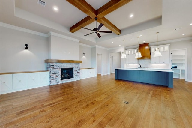 unfurnished living room featuring ceiling fan, beam ceiling, coffered ceiling, light hardwood / wood-style floors, and a brick fireplace