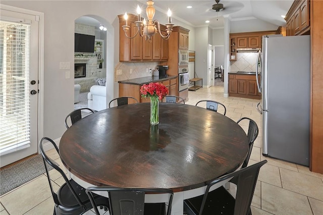 tiled dining space with a fireplace, lofted ceiling, ceiling fan with notable chandelier, and crown molding