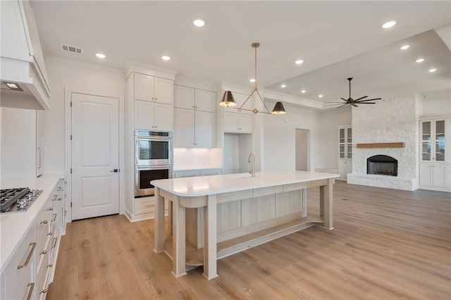 kitchen featuring decorative light fixtures, an island with sink, a breakfast bar area, white cabinets, and stainless steel appliances