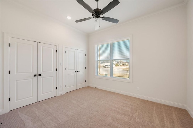 unfurnished bedroom featuring multiple closets, light colored carpet, ornamental molding, and ceiling fan