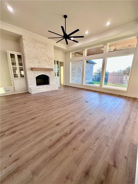 unfurnished living room featuring ceiling fan, wood-type flooring, ornamental molding, and a fireplace